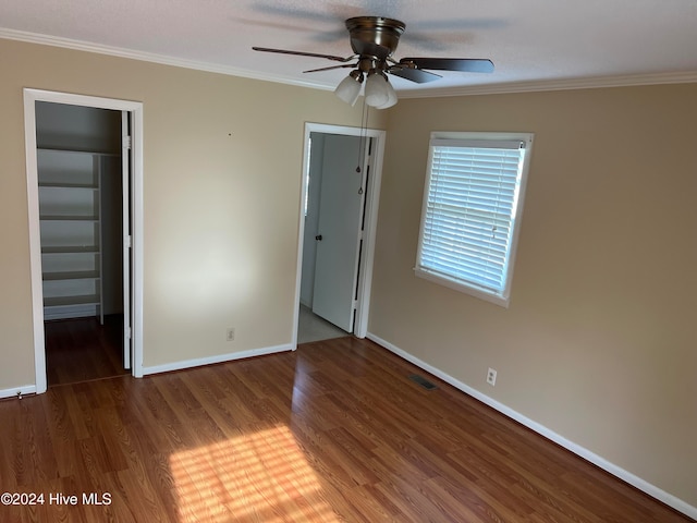 unfurnished bedroom featuring a walk in closet, crown molding, ceiling fan, dark hardwood / wood-style floors, and a closet