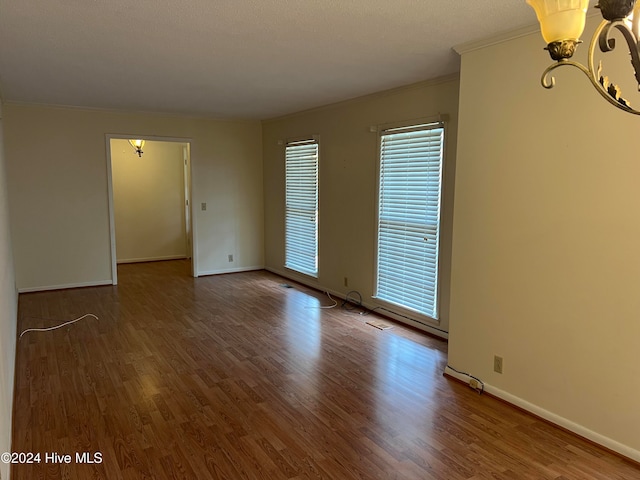 empty room with a chandelier, wood-type flooring, and ornamental molding