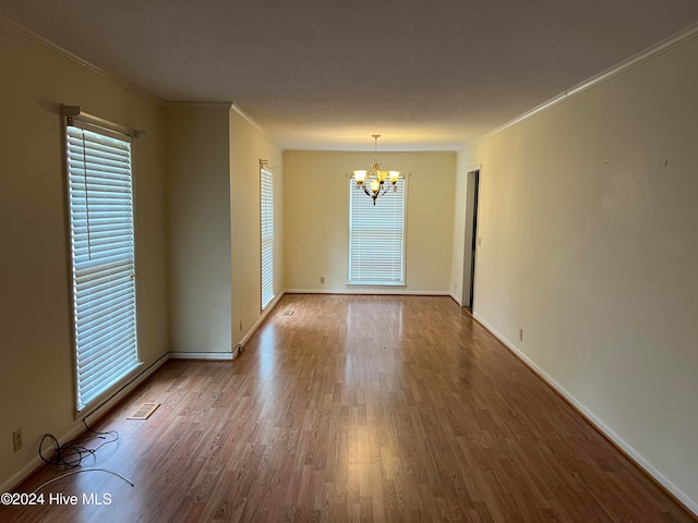 spare room with hardwood / wood-style flooring, ornamental molding, and a chandelier