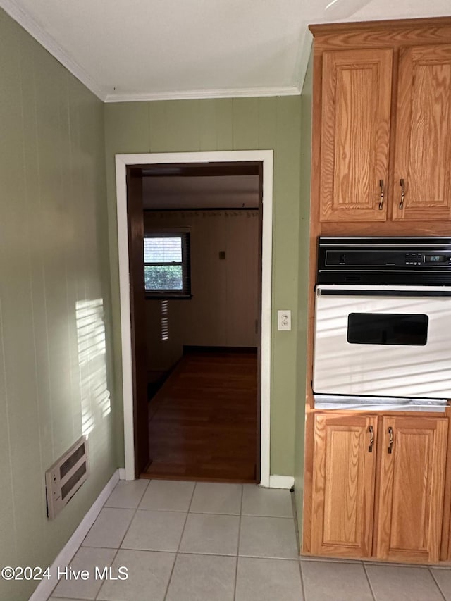 kitchen with light tile patterned flooring, ornamental molding, brown cabinetry, and white oven