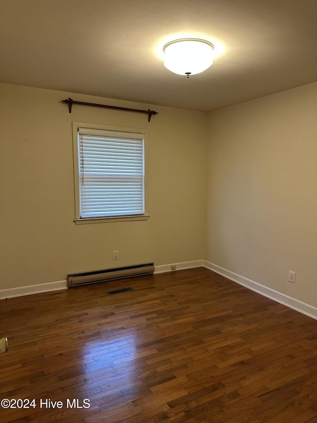 spare room featuring a baseboard heating unit, dark wood-style flooring, visible vents, and baseboards