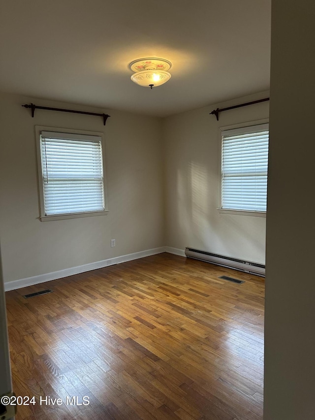 unfurnished room with baseboards, visible vents, baseboard heating, and wood finished floors