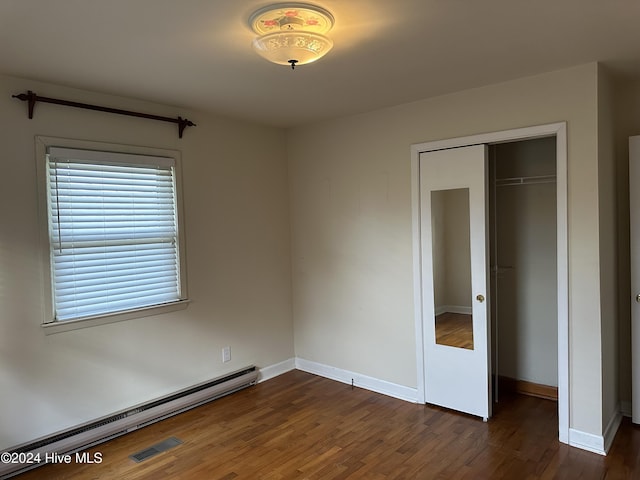 unfurnished bedroom with a baseboard heating unit, dark hardwood / wood-style floors, and a closet