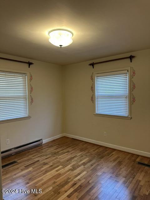 spare room with a baseboard radiator, visible vents, baseboards, and wood finished floors