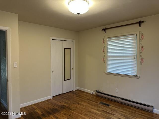 unfurnished bedroom with dark wood-type flooring, baseboards, baseboard heating, and a closet