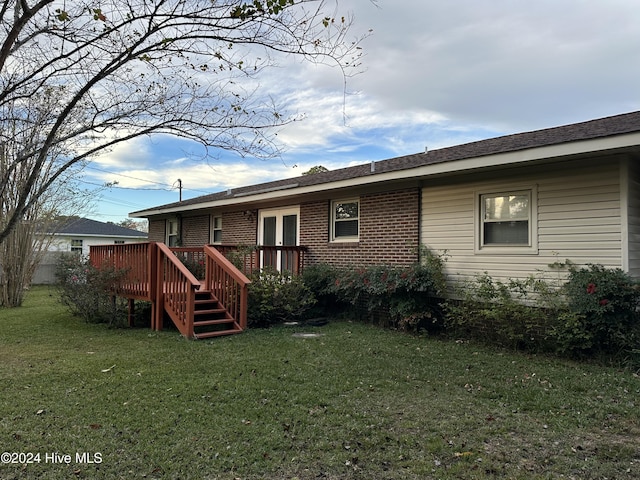 back of property with brick siding, a lawn, a deck, and stairs