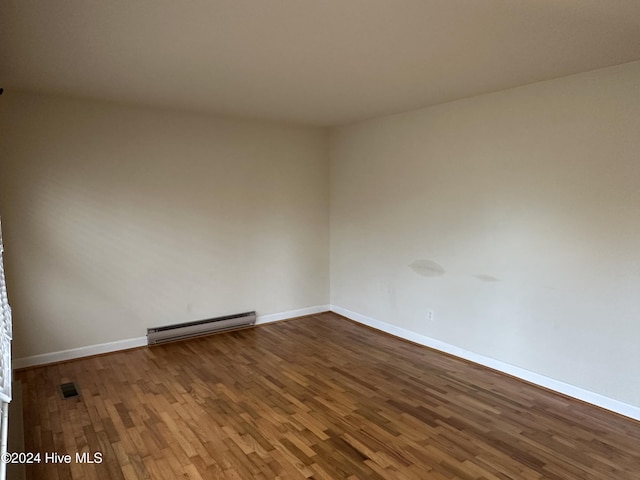 unfurnished room with baseboards, visible vents, a baseboard heating unit, and wood finished floors