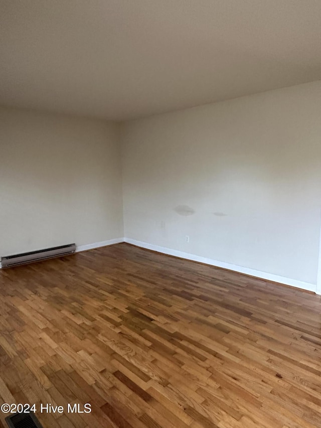 unfurnished room with a baseboard heating unit, baseboards, and wood finished floors