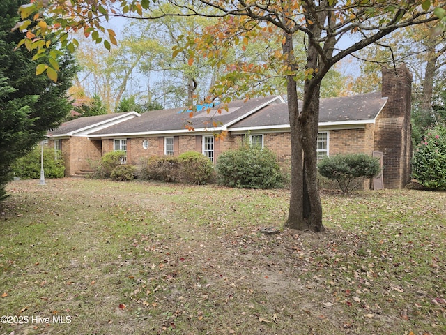 view of front facade with a front yard, a chimney, and brick siding