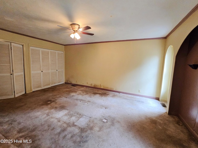 unfurnished bedroom featuring baseboards, arched walkways, two closets, and ornamental molding