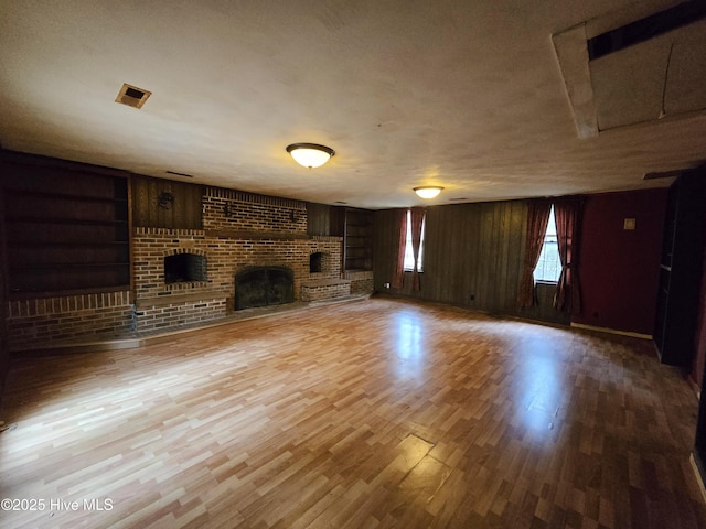 unfurnished living room with a textured ceiling, built in shelves, wood finished floors, visible vents, and a brick fireplace