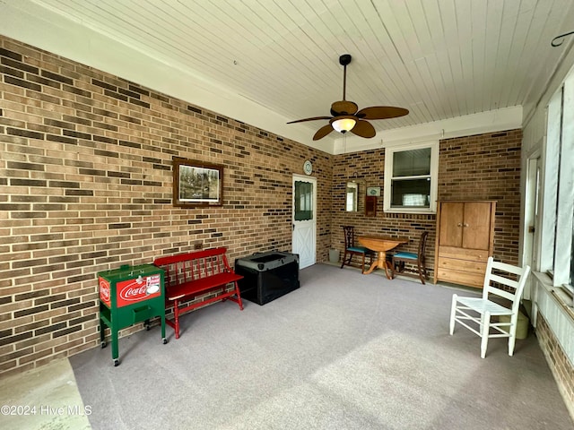 living area featuring wood ceiling, ceiling fan, carpet floors, and brick wall