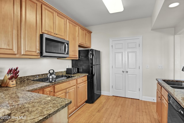 kitchen with sink, black appliances, dark stone counters, and light wood-type flooring