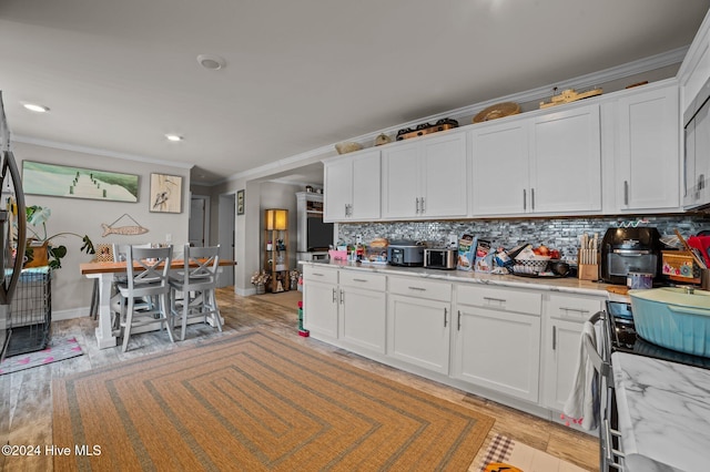 kitchen featuring white cabinetry, light stone countertops, ornamental molding, decorative backsplash, and light wood-type flooring