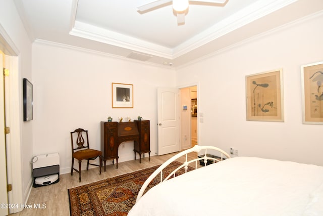 bedroom featuring light wood-type flooring, a raised ceiling, ceiling fan, and crown molding