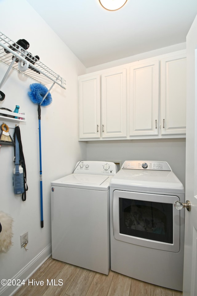 washroom with washing machine and clothes dryer, light hardwood / wood-style flooring, and cabinets