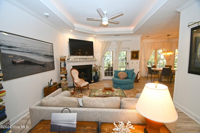 living room featuring ceiling fan with notable chandelier, a raised ceiling, ornamental molding, and light hardwood / wood-style flooring