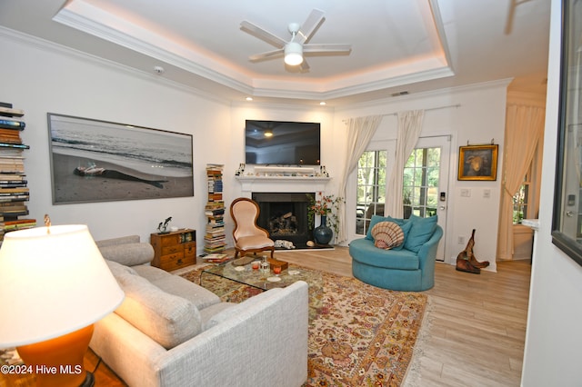 living room featuring a tray ceiling, ceiling fan, ornamental molding, and light wood-type flooring