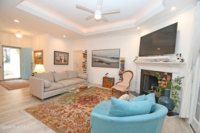 living room with a tray ceiling, crown molding, light hardwood / wood-style flooring, and ceiling fan