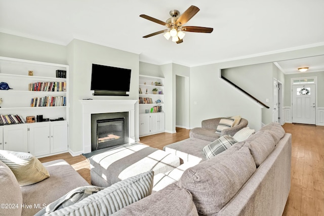 living room featuring ceiling fan, ornamental molding, built in shelves, and light hardwood / wood-style flooring