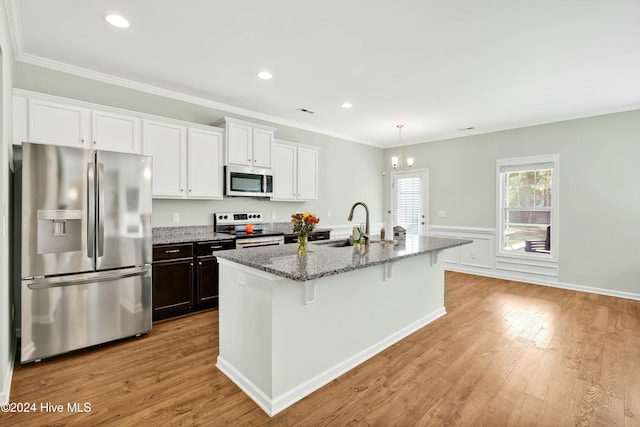 kitchen featuring appliances with stainless steel finishes, light wood-type flooring, an island with sink, and dark stone countertops