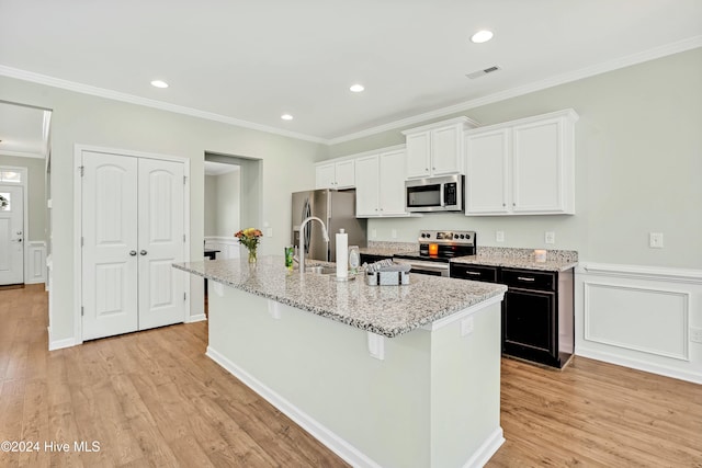 kitchen featuring a center island with sink, light wood-type flooring, ornamental molding, light stone counters, and stainless steel appliances