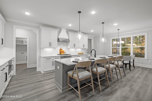 kitchen with white cabinetry, hanging light fixtures, wall chimney exhaust hood, and a kitchen island with sink