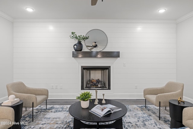 sitting room featuring ceiling fan, wood walls, hardwood / wood-style floors, a fireplace, and ornamental molding