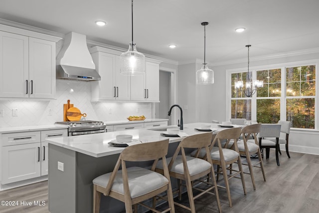 kitchen with white cabinetry, wall chimney exhaust hood, stainless steel range with gas cooktop, an island with sink, and pendant lighting