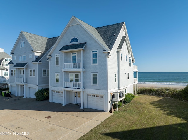 view of front facade featuring a front yard, a balcony, a water view, and a view of the beach