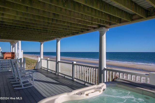 deck with a view of the beach, a water view, and an outdoor hot tub