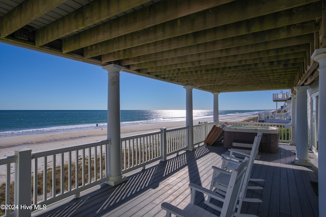 wooden deck with a beach view, a water view, and a hot tub