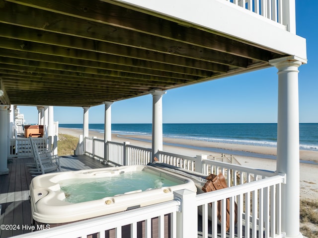 wooden terrace featuring an outdoor hot tub, a water view, and a beach view