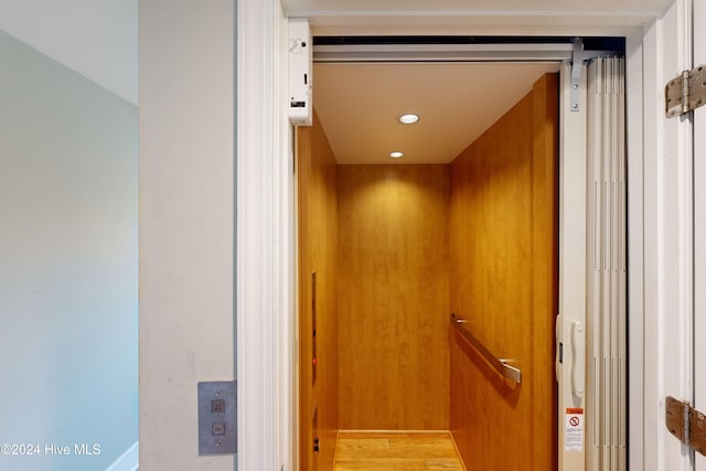 interior details featuring hardwood / wood-style flooring, elevator, and wooden walls