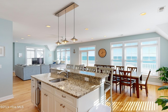 kitchen featuring light wood-type flooring, sink, decorative light fixtures, white cabinetry, and an island with sink