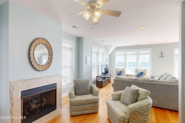 living room featuring a tile fireplace, ceiling fan, and light hardwood / wood-style floors