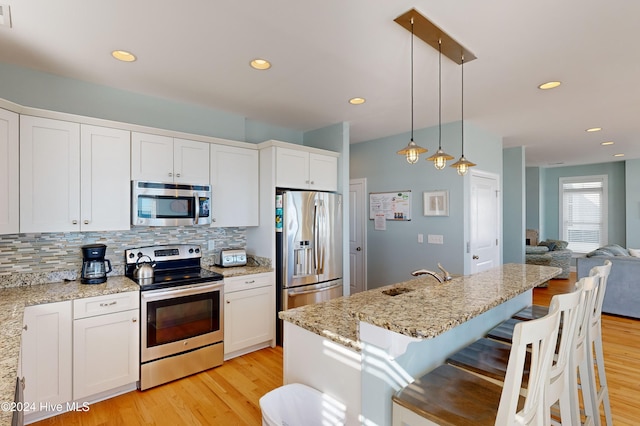 kitchen featuring sink, light hardwood / wood-style flooring, pendant lighting, white cabinets, and appliances with stainless steel finishes