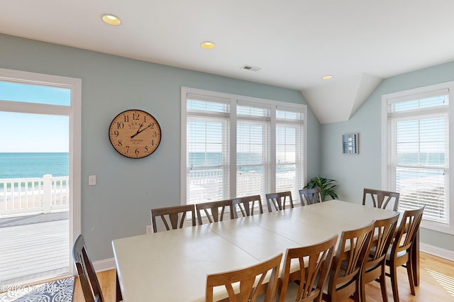 dining area featuring light hardwood / wood-style floors, a water view, and lofted ceiling