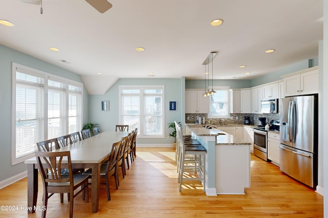 kitchen featuring white cabinets, decorative light fixtures, light wood-type flooring, and stainless steel appliances