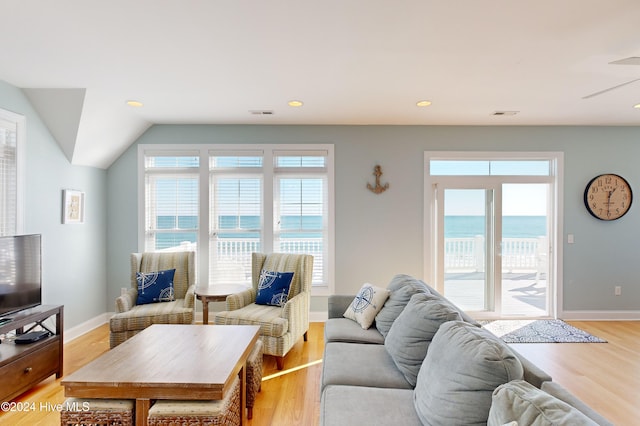 living room with vaulted ceiling, a water view, light hardwood / wood-style flooring, and a healthy amount of sunlight