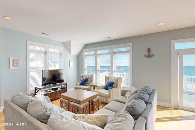 living room featuring a water view, light wood-type flooring, and vaulted ceiling