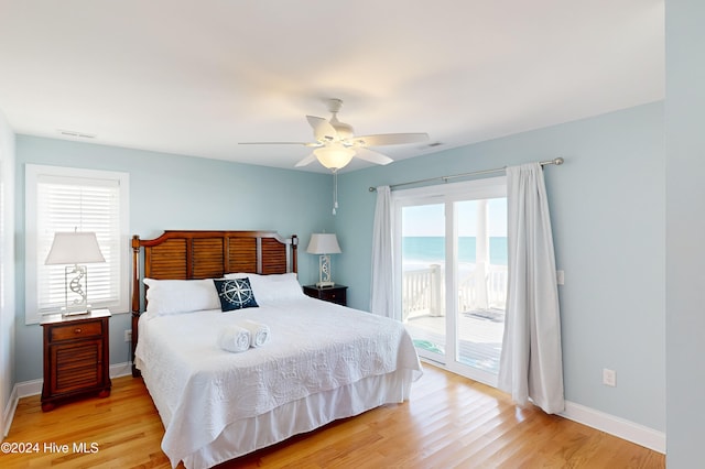 bedroom featuring access to outside, multiple windows, a water view, and light hardwood / wood-style floors