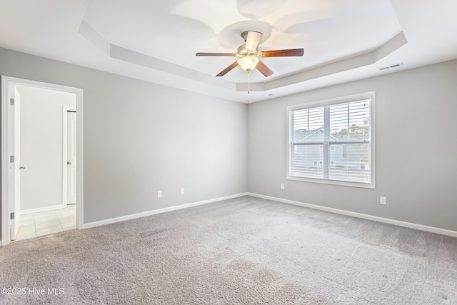 empty room with ceiling fan, light carpet, and a tray ceiling