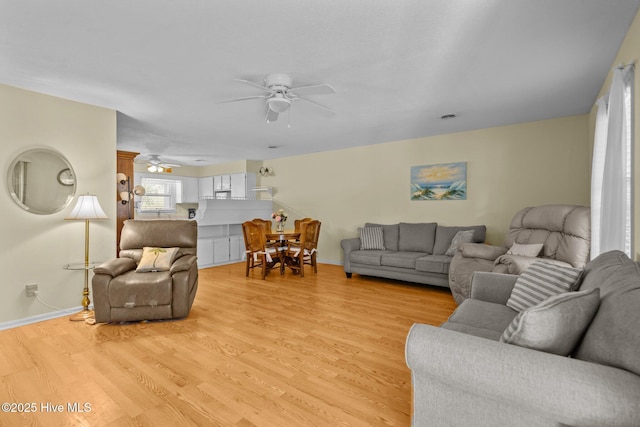 living area with light wood-style floors, baseboards, and a ceiling fan