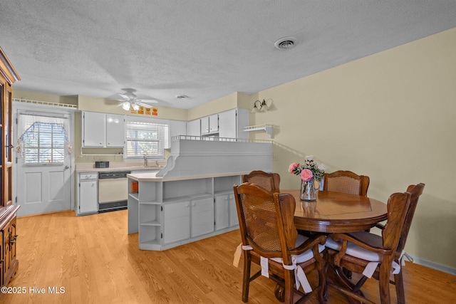 dining room with light wood finished floors, a ceiling fan, visible vents, and a textured ceiling