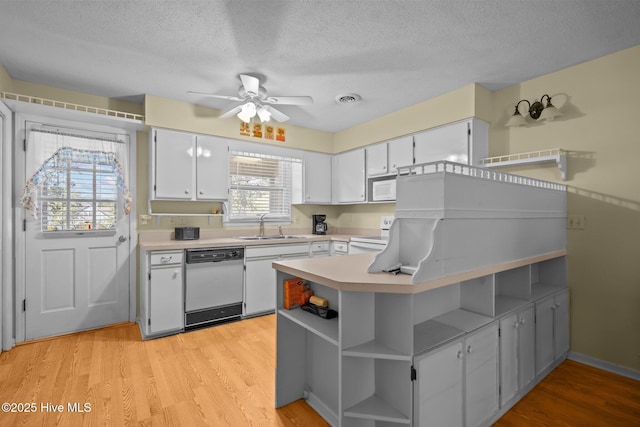 kitchen with a peninsula, white appliances, a sink, light countertops, and open shelves