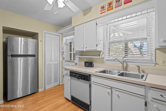 kitchen with dishwasher, freestanding refrigerator, light countertops, white cabinetry, and a sink