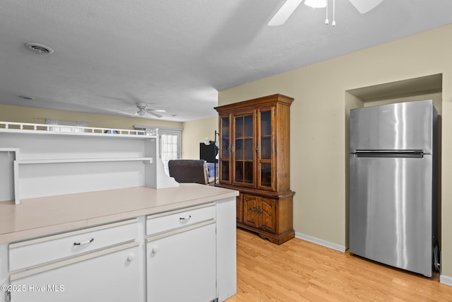 kitchen with light countertops, light wood-style floors, freestanding refrigerator, a ceiling fan, and white cabinets