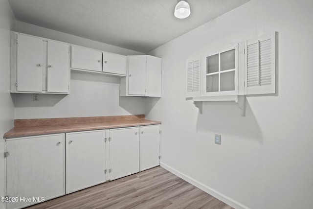 kitchen featuring light wood finished floors, baseboards, white cabinets, light countertops, and a textured ceiling