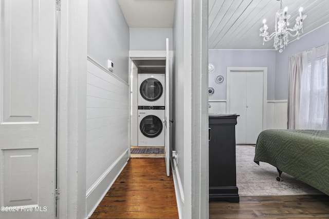 clothes washing area with dark wood-type flooring, an inviting chandelier, stacked washer and clothes dryer, and crown molding